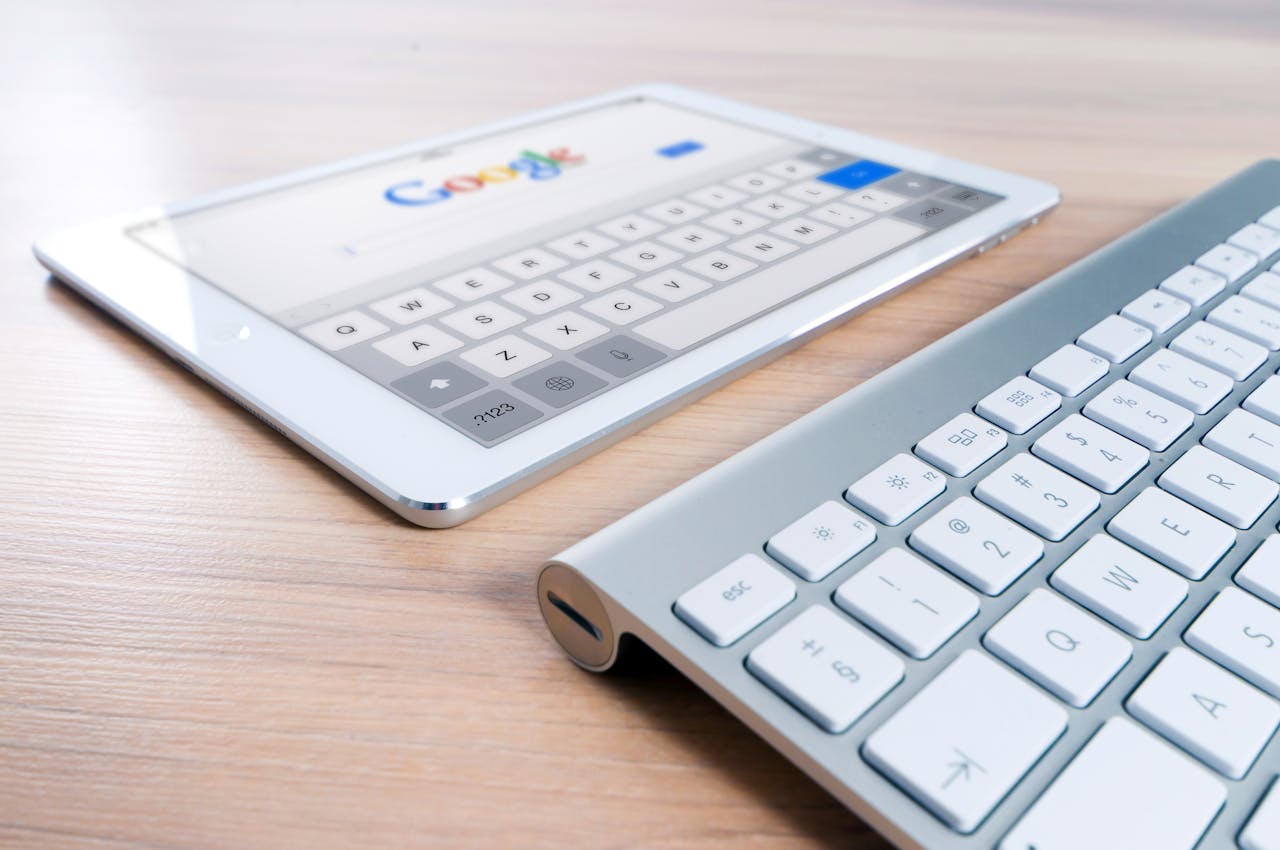 hero-img A modern tablet displaying a search engine logo next to a wireless keyboard on a wooden desk.